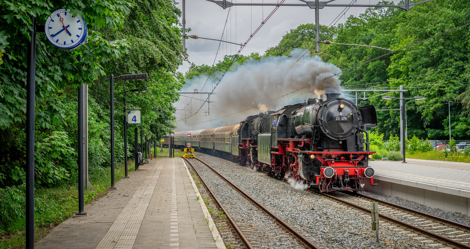 Stoomlocomotief 23 076 komt met rijtuigen onder stoom door een station